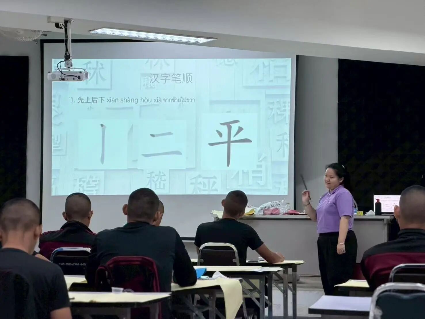 ตำรวจนั่งเรียนเขียนอักษรจีนโดยมีครูสอนหน้าจอ