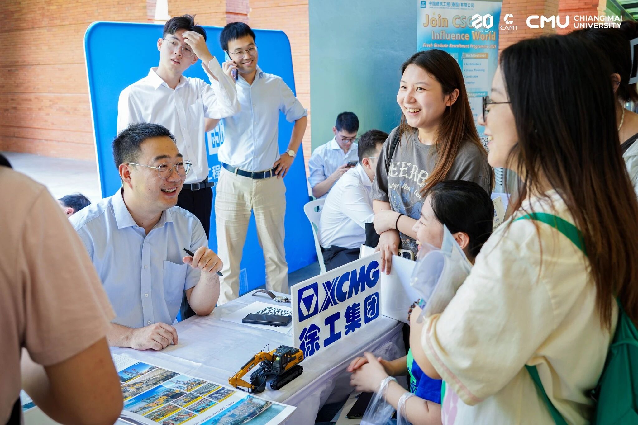 นักศึกษาพูดคุยกับตัวแทนบริษัทจีนที่โต๊ะรับสมัครงานในงานนัดพบแรงงานที่ มช.